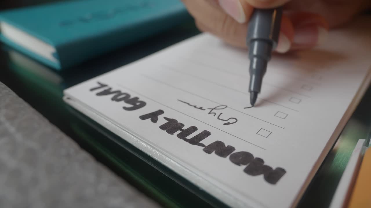 Primo piano di mano che scrive gli obiettivi mensili su un taccuino