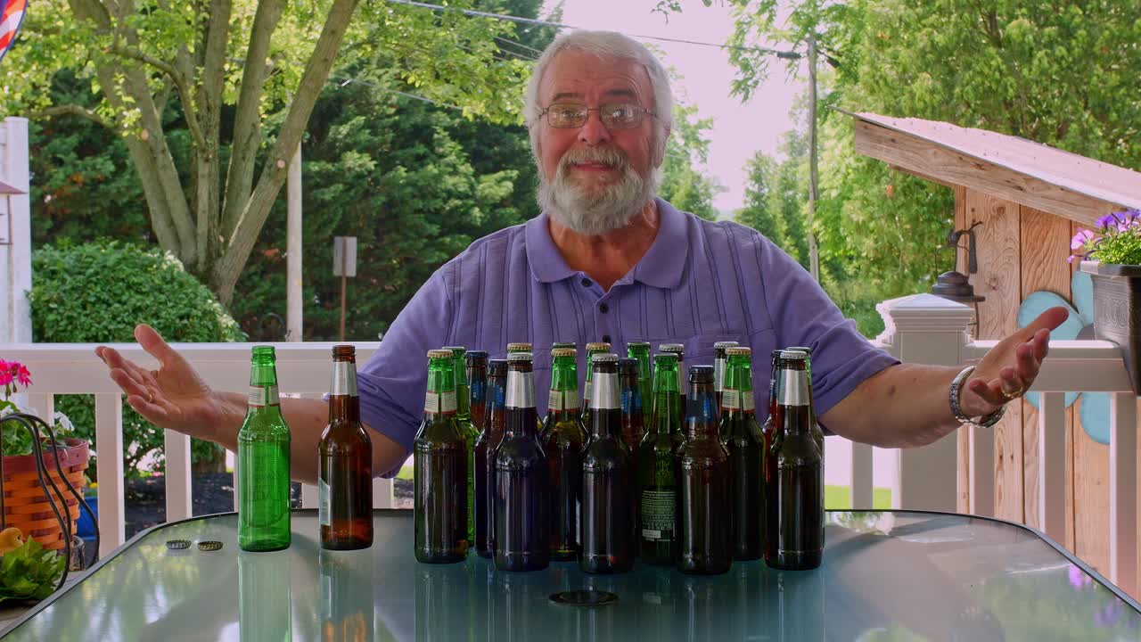 A man sits at a table outdoors surrounded by various beer bottles. He describes and reacts to the flavors while enjoying the sunny weather and a relaxed atmosphere