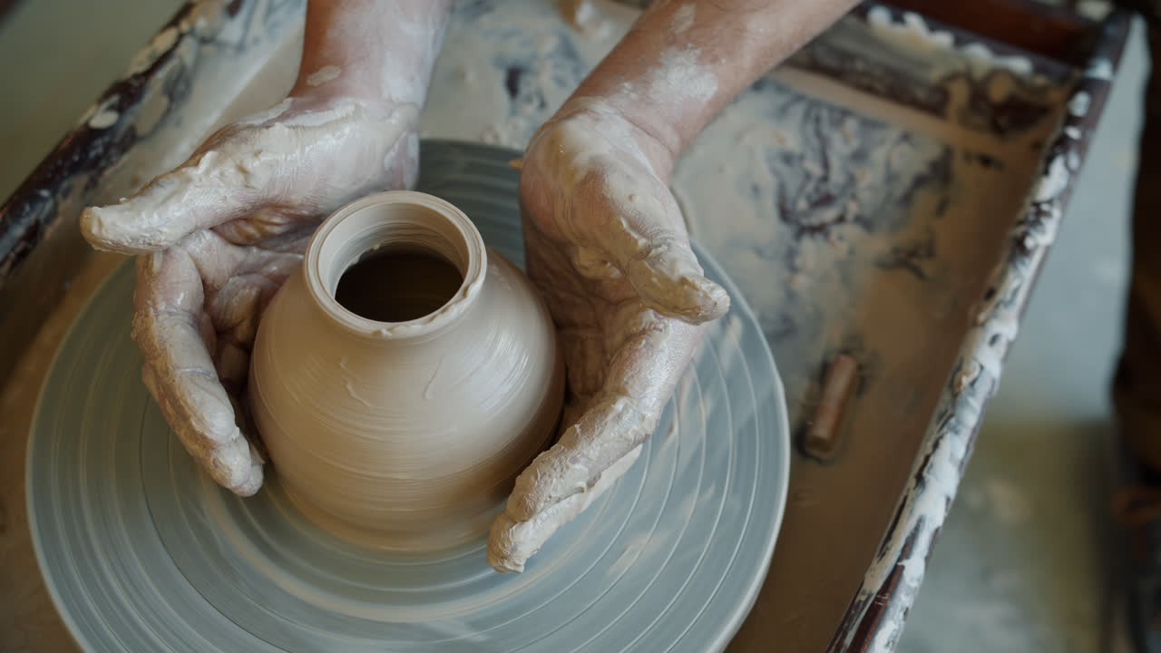Hands shaping a clay pot on a pottery wheel