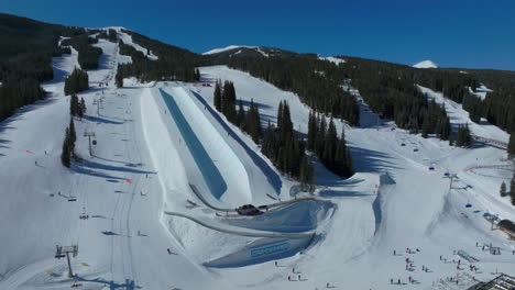 drone aéreo cobre montaña invierno esquí snowboard resort medio tubo entrenamiento práctica trucos competencia colorado temprano por la mañana luz del sol nieve fresca ascensor de esquí multitud cinematográfica pan a la derecha movimiento 4k
