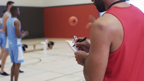 entrenamiento diverso del equipo de baloncesto masculino y el entrenador tomando notas en la cancha cubierta, en cámara lenta
