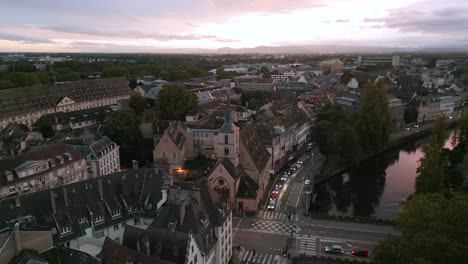 aerial sunset view over strasbourg’s old town, with warm pink skies reflecting on the canal and evening lights beginning to glow across the charming historic rooftops and narrow streets