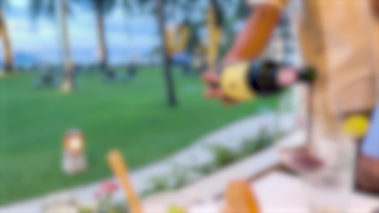 A sommelier pours wine in an outdoor dining setting with a blurred background, creating a relaxed and elegant atmosphere