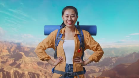 asian female hiker with mountaineering backpack smiling and posing arms akimbo while traveling at the top of mountain