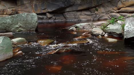 Tilting-down-4K-shot-of-a-crimson-mineral-filled-river-coming-from-the-Mosquito-Falls-surrounded-by-rocks-and-cliffs-in-the-Chapada-Diamantina-National-Park-in-Northeastern-Brazil-on-a-summer-day