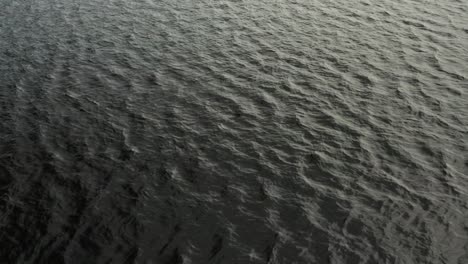 Aerial,-very-dark-lake-water-with-gentle-waves-rippling-during-the-day