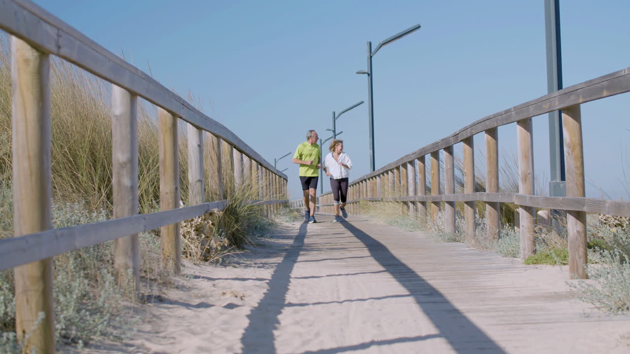 Cheerful man and woman running along wooden path on summer day