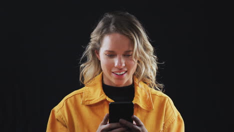 Foto-De-Estudio-De-Una-Mujer-Transmitiendo-Contenido-En-Un-Teléfono-Móvil-Y-Sonriendo-En-Cámara-Lenta