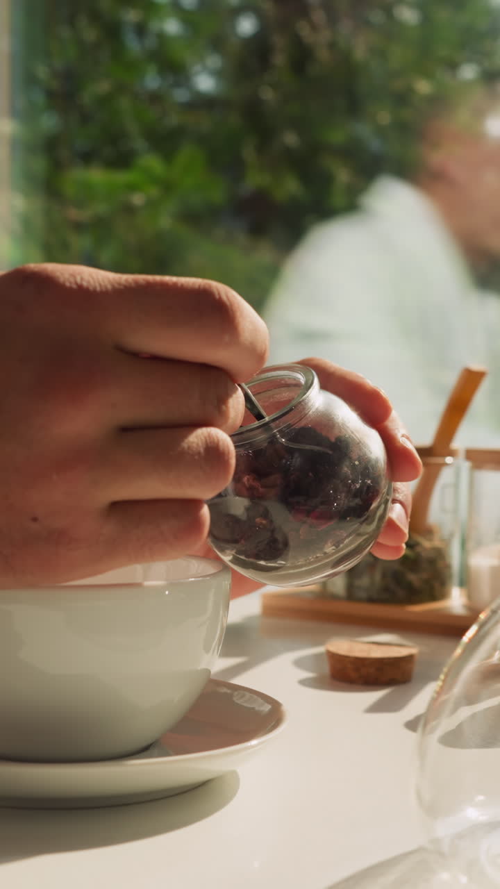 Man uses teaspoon taking tea out of glass jar. Man tries preparing natural tea in morning at breakfast time. Enjoying herbal infusion for good health