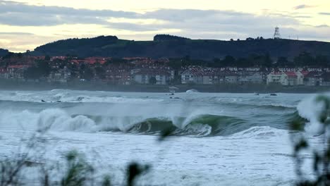 Grandes-Olas-Rompiendo-En-El-Mar-Con-La-Ciudad-De-Fondo