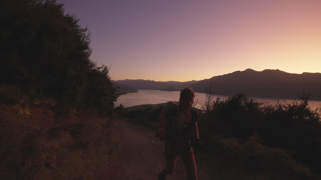 Donna che pratica nordic walking su un ripido sentiero di montagna con il bagliore dell'alba nel cielo.