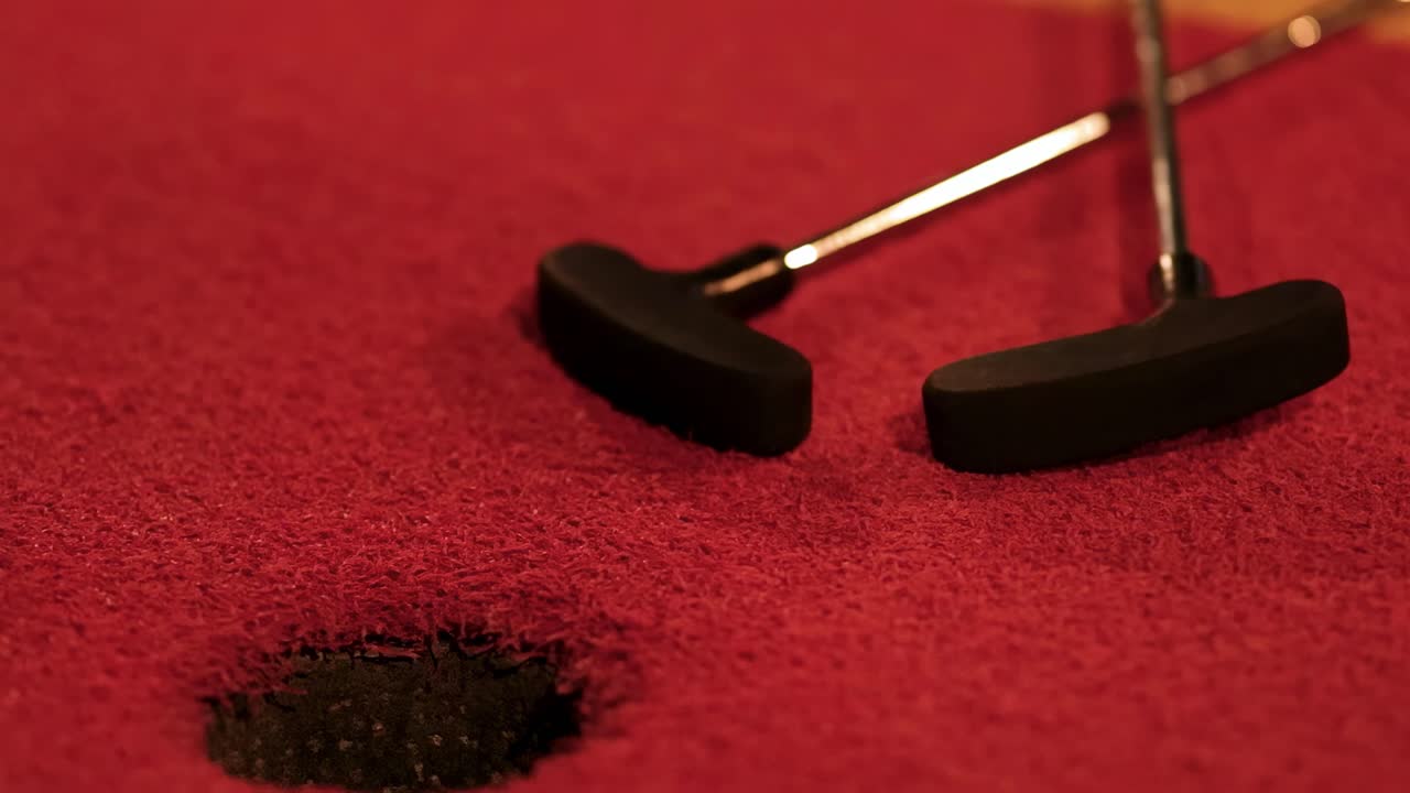 Primo piano di un putter vicino a una buca su una superficie di un campo da minigolf rosso.