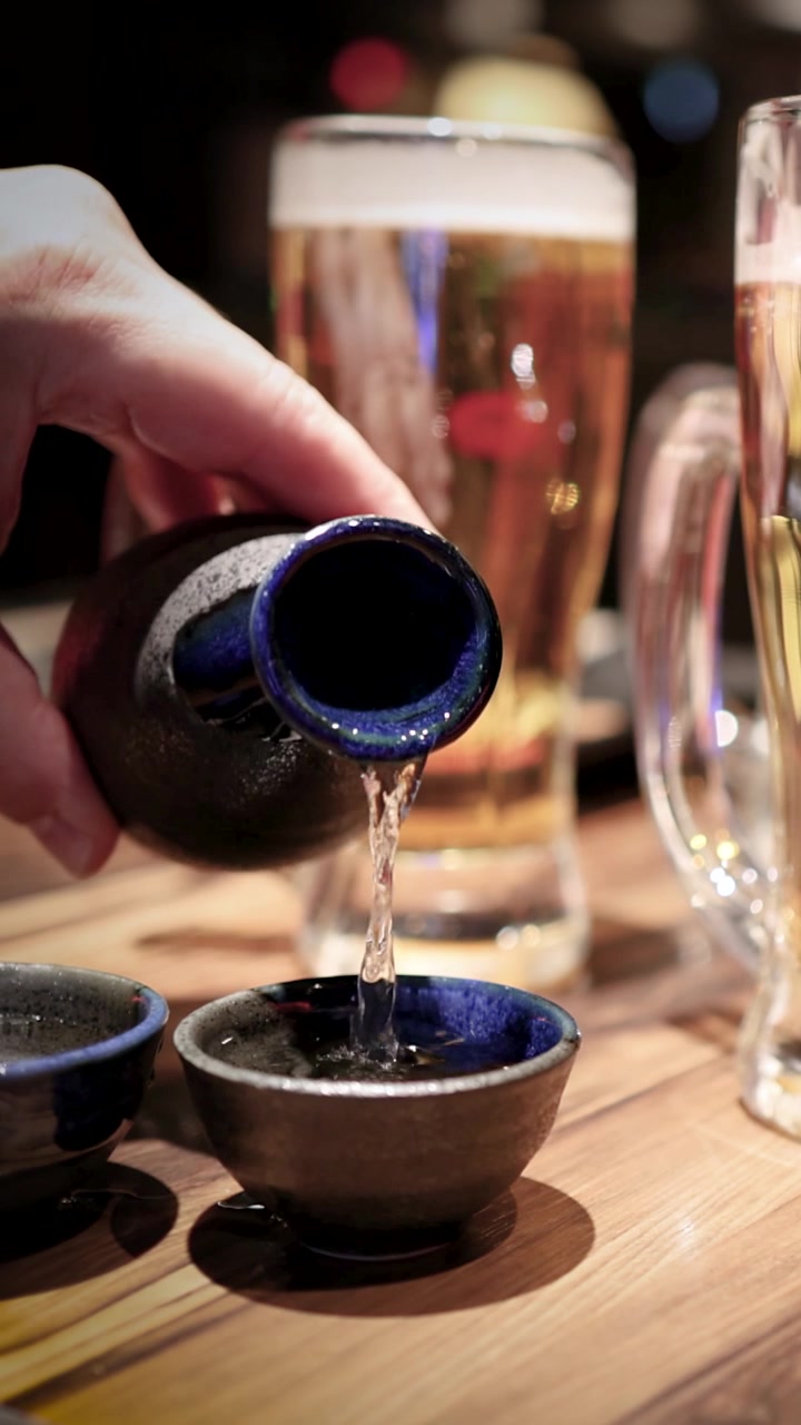 Tangan Menuangkan Sake Tradisional Jepang ke dalam Cangkir Keramik Kecil