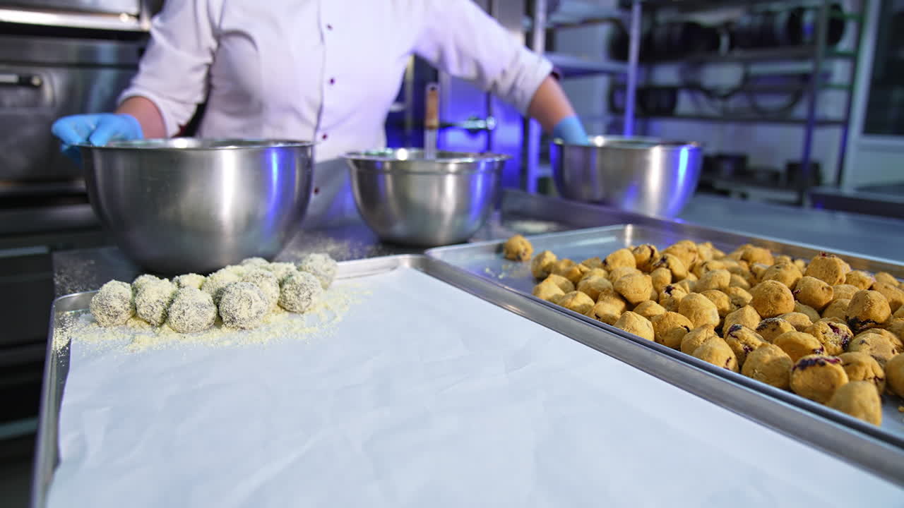 Cookies being coated with sprinkling. Worker shaking metal bowl in hands to cover all sweets with coconut flakes.