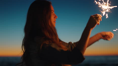 young woman playing with sparklers on beach at sunset celebrating new years eve waving sparkler fireworks enjoying independence day celebration by the sea