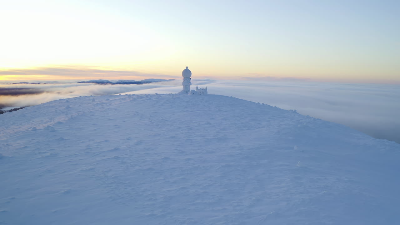 Drone circling a weather radar on the snowy Luostotunturi fell in Lapland, sunset