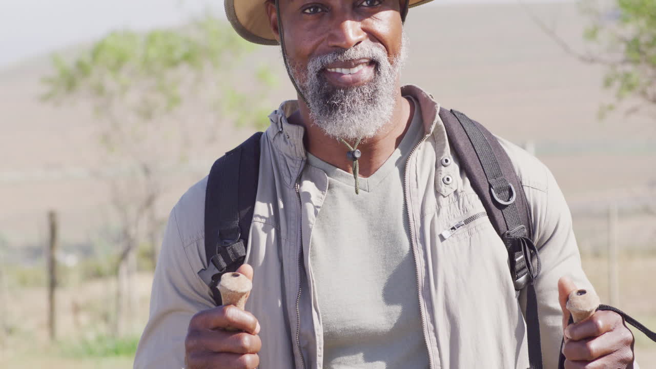 Portrait of happy senior african american man hiking with trekking poles on sunny day, slow motion