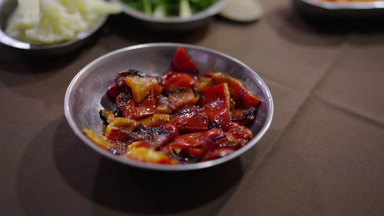 Rotating closeup macro shot featuring cooked red bell pepper on aluminum bowl over table among other sides for classic cuisine.