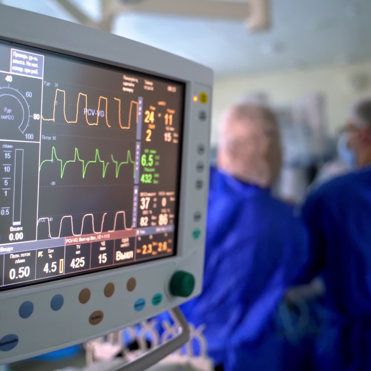 Hospital monitor in the operating room. Screen shows vital signs of a patient on the background of surgical procedure. Teamwork of doctors.