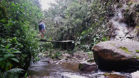 un excursionista caucásico cruza un puente colgante sobre un pequeño río de la selva