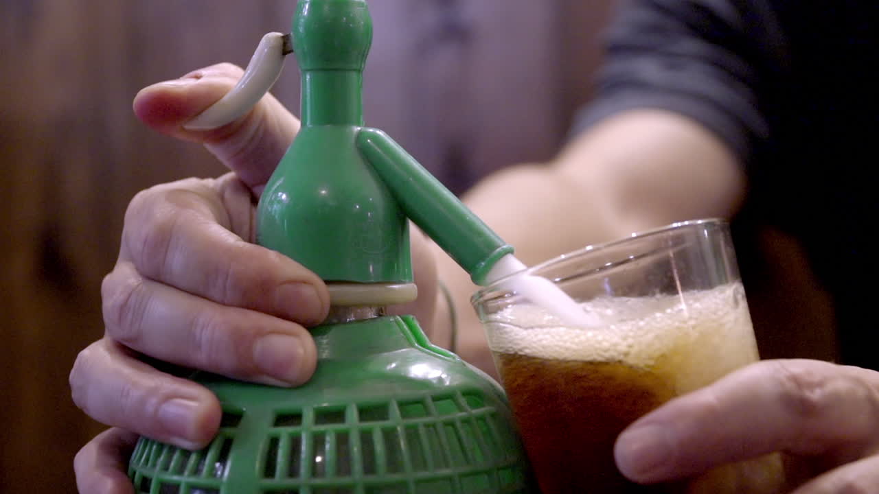 A person using a vintage soda siphon to prepare a fizzy drink