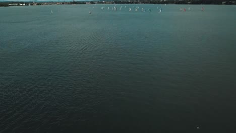 A-shot-of-deep-lake-water-tilts-up-to-reveal-a-sailboat-regatta-on-a-beautiful-day