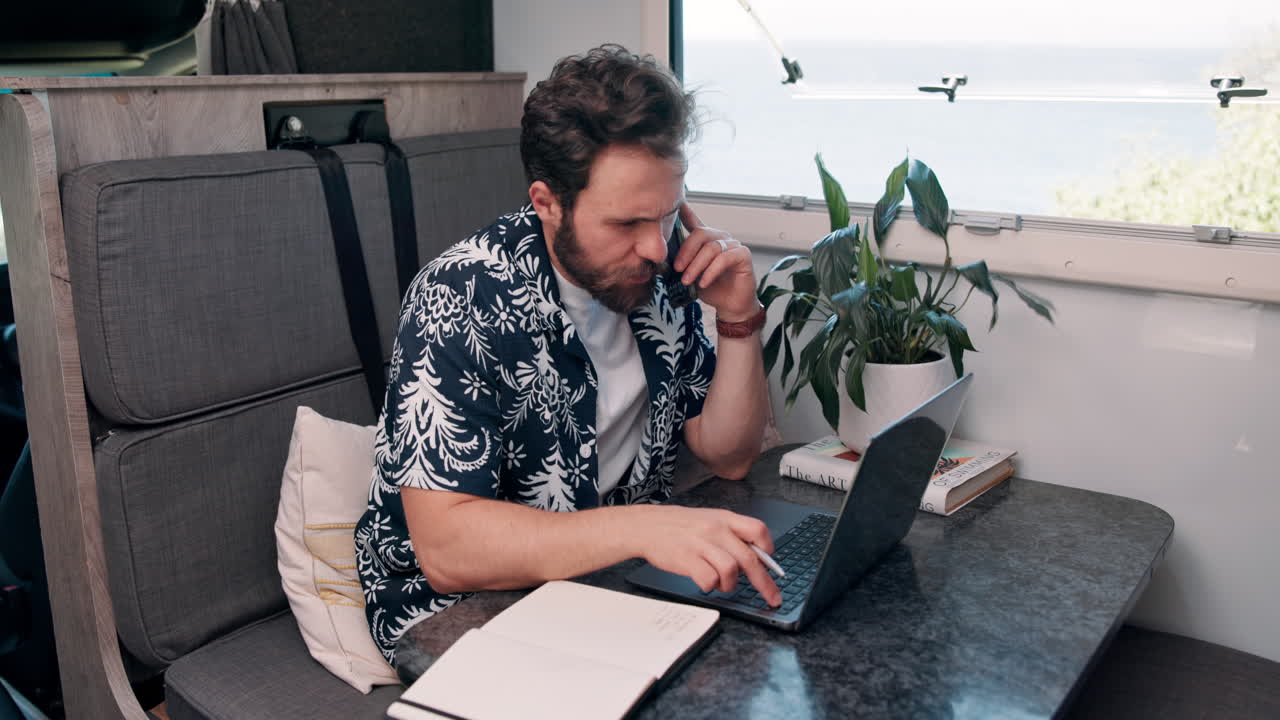 Mand taler i telefon og arbejder på bærbar computer i autocamper