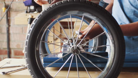 pre teen boy using a spanner to attach a wheel to his racing kart, mid section detail, seen through spokes of a wheel