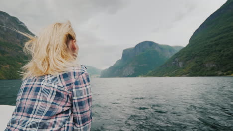 a romantic woman on the bow of the ship sailing along the beautiful fjord the wind blows into her ha