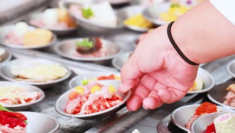 una mano selecciona dim sum de una vibrante variedad de platos en un bullicioso mercado de phuket, mostrando delicias culinarias locales
