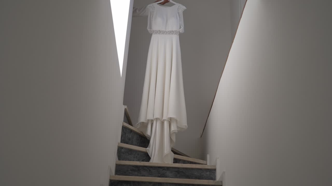 vestido de novia blanco colgado en una escalera estrecha, iluminado por la luz natural
