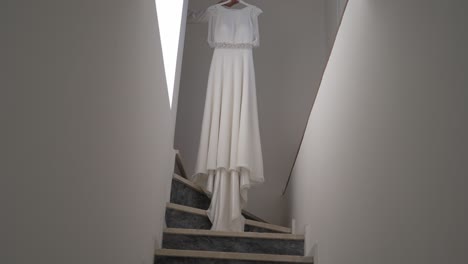 white wedding dress hanging in a narrow stairway, illuminated by natural light