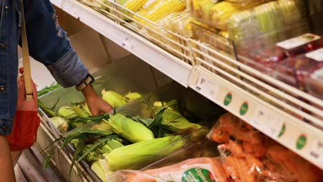 a person picks corn from a supermarket shelf under bright lighting, showcasing fresh produce selection
