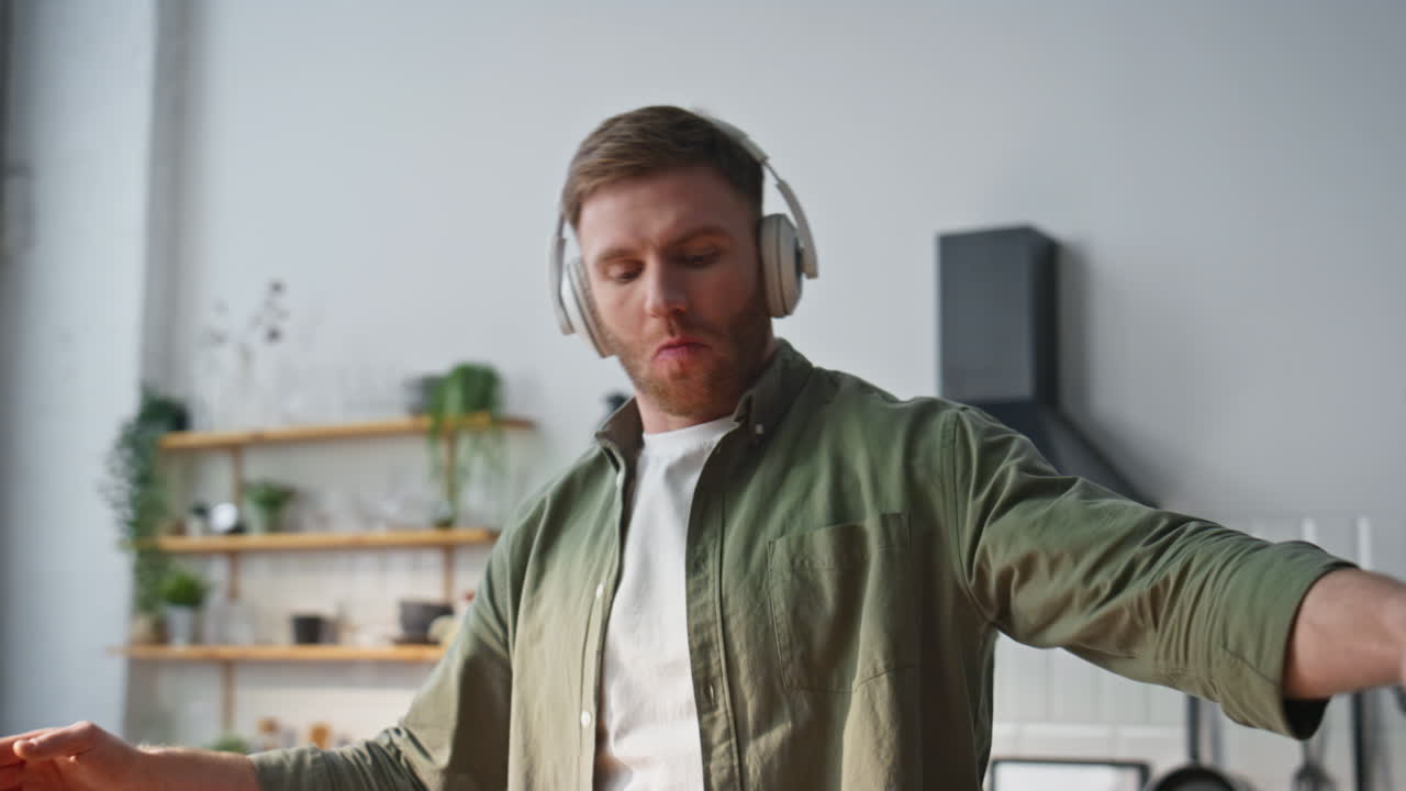 Dancing man cooking breakfast at apartment kitchen wearing headphones closeup