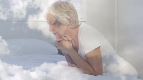 Animation-of-caucasian-senior-woman-praying-over-moving-clouds