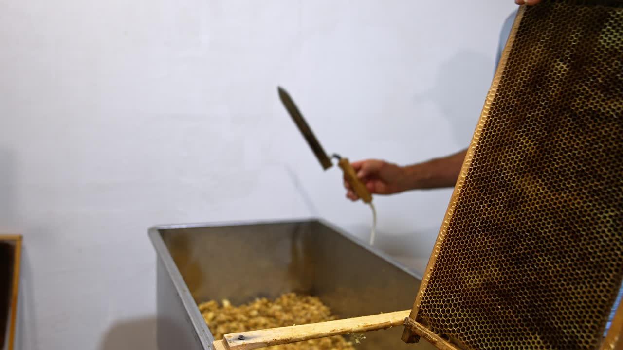 Unrecognized man takes the frame and electric knife. Apiculturist cleans off the wax from wooden frame. Close up.