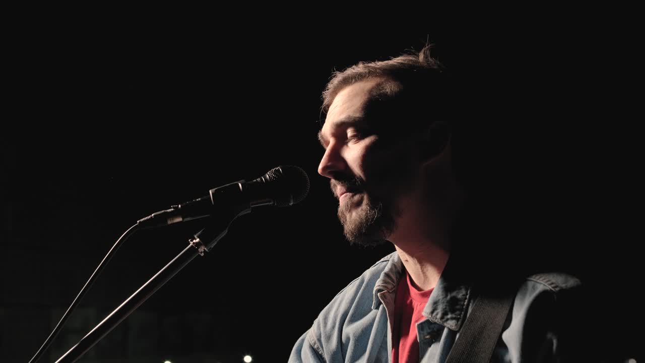 un músico está tocando la guitarra en un gran escenario con miembros de la audiencia sosteniendo linternas en el fondo. el auditorio está lleno de hermosas luces parpadeantes.