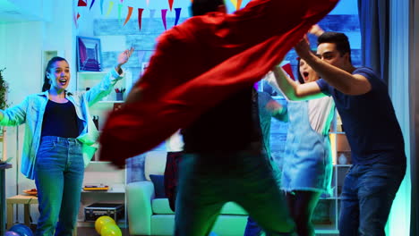 un joven guapo llega a la fiesta con una capa roja de superhéroe.
