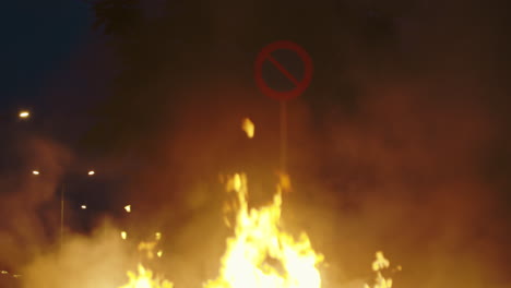 large fire and smoke at night with obscured road sign