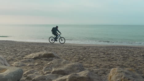 Mann-Fährt-In-Den-Morgenstunden-Mit-Dem-Fahrrad-Am-Ruhigen-Sandstrand-Entlang