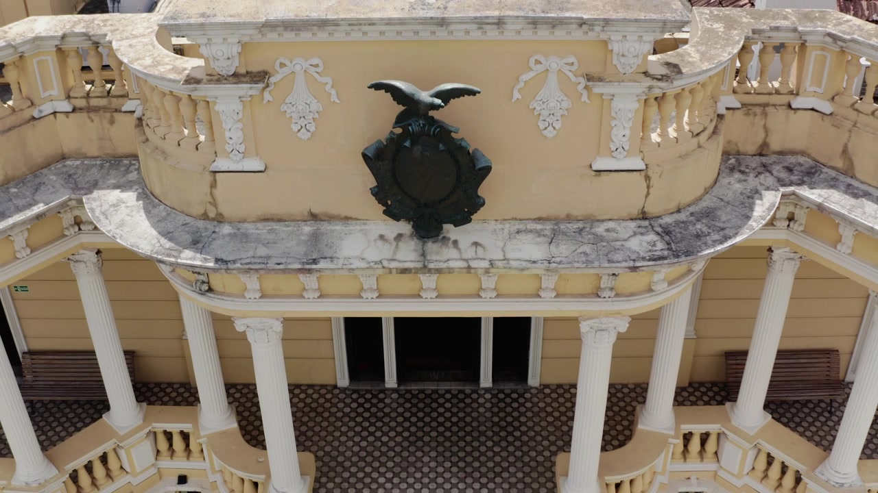 Ripresa aerea ravvicinata del portico del Palacio Rio Negro, colonne bianche e balaustre, che si alza verso una vista dall'alto del pavimento piastrellato, tetti in terracotta e torre, giornata di sole, Manaus, Brasile 4K