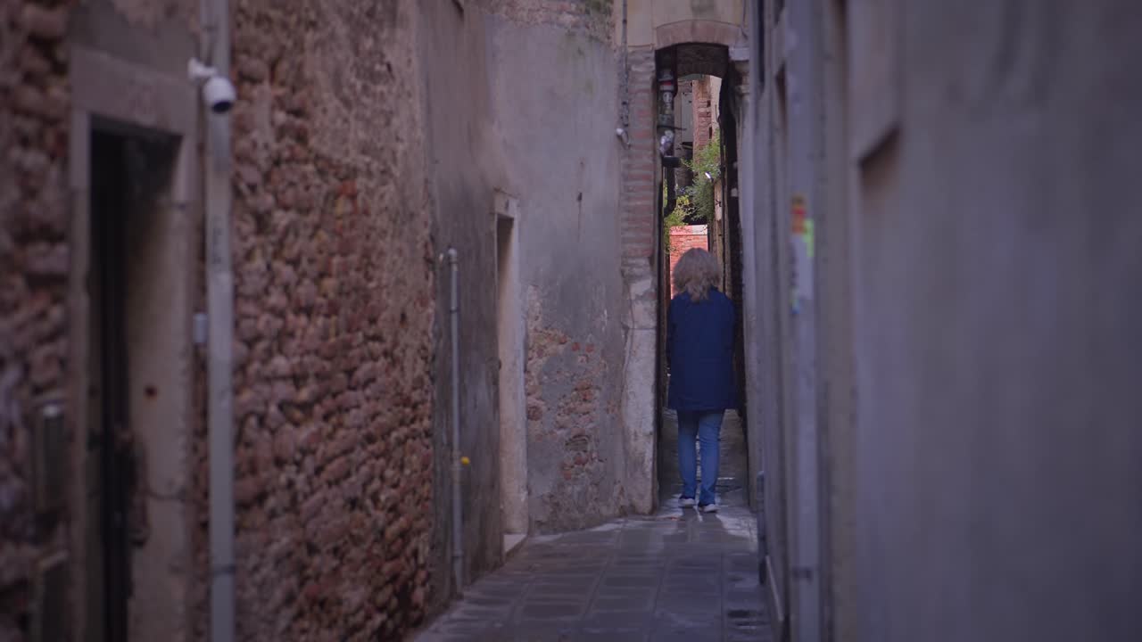 Una donna cammina da sola lungo la stretta e scarsamente illuminata strada di un vicolo urbano