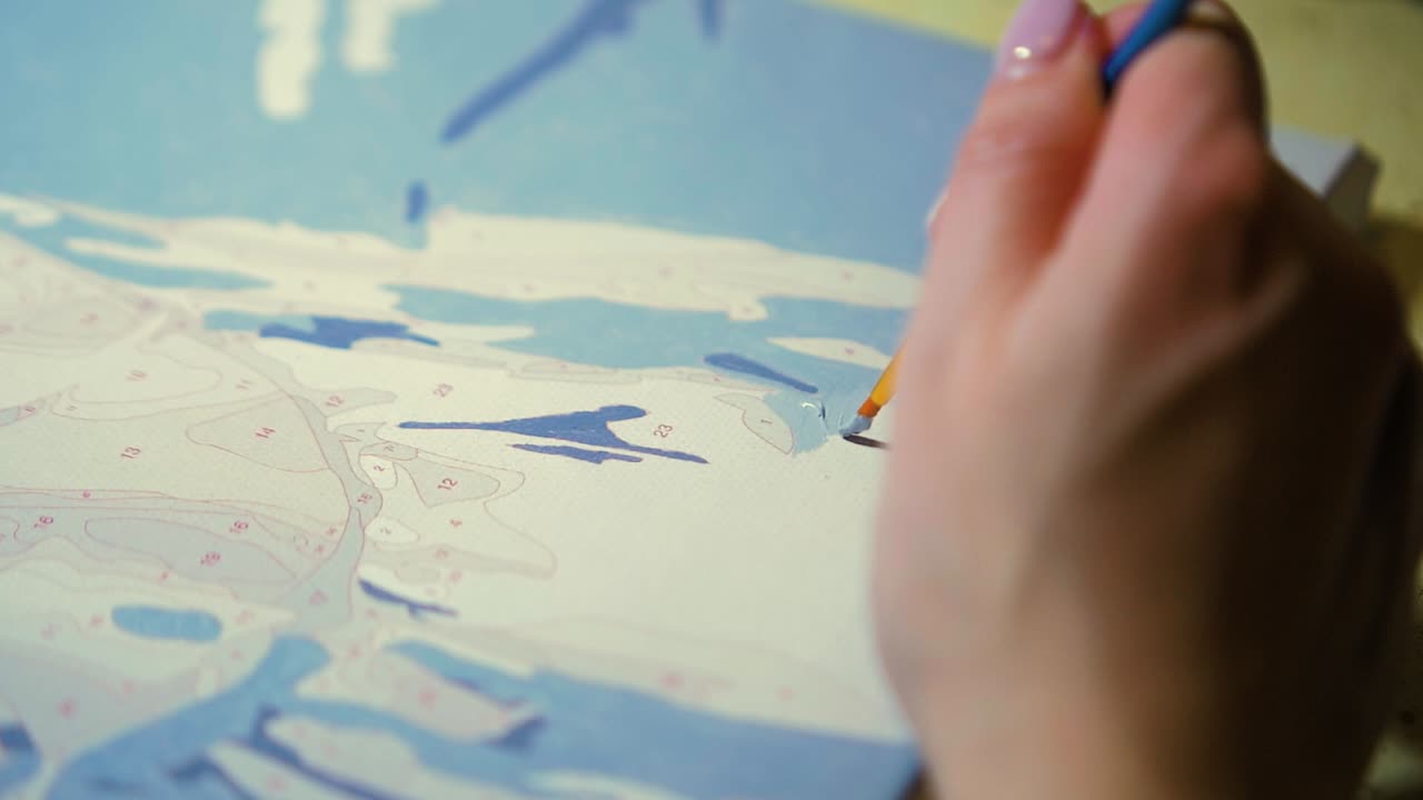 ペイントブラシを持ち、キャンバステンプレートにライトグレーのアクリルペイントで絵を描く女性アーティストの接写、スローモーションショットの接写