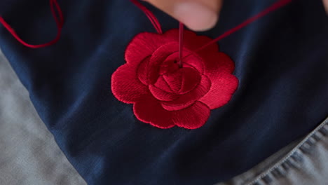 close-up of hand embroidering a red rose on fabric