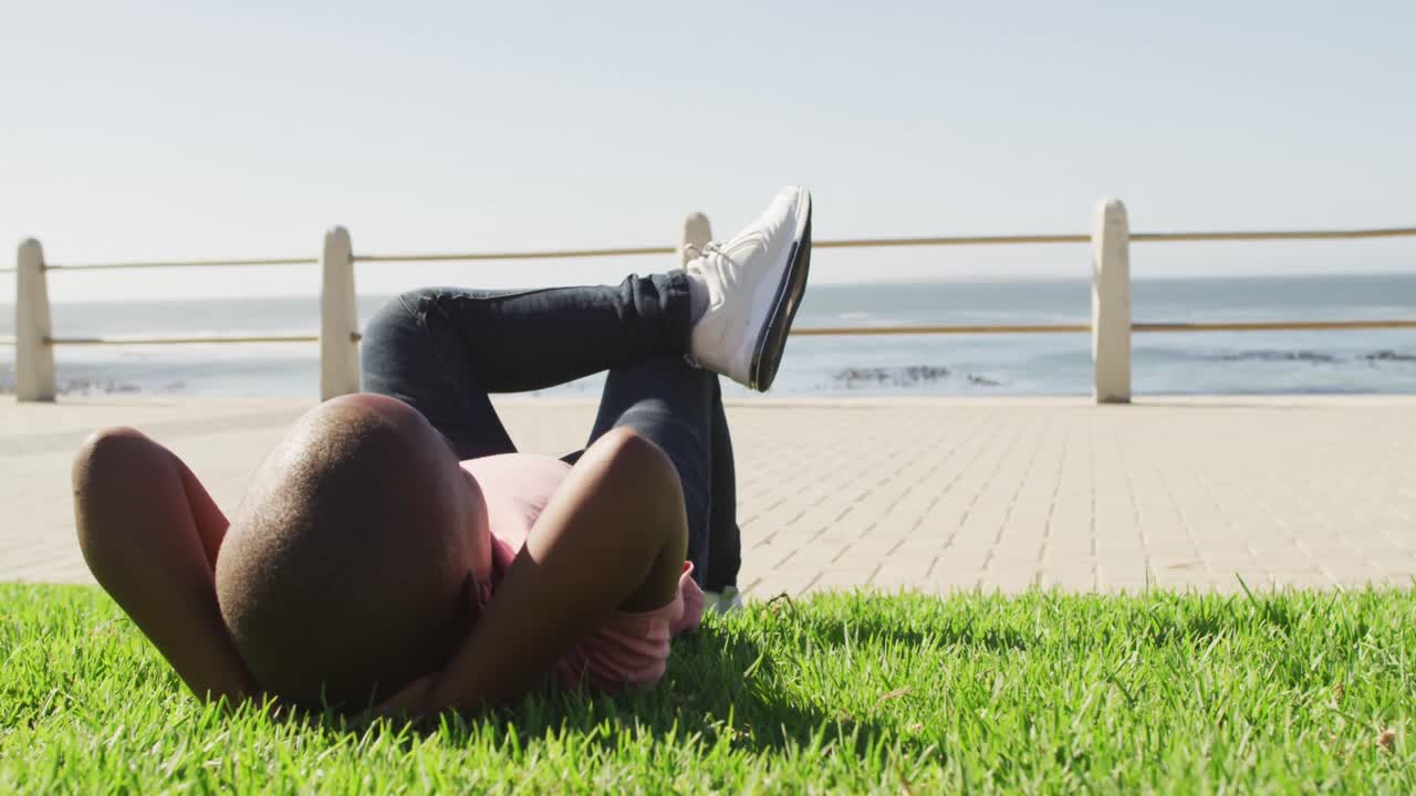 video de un feliz niño afroamericano acostado en la hierba, relajándose junto al mar