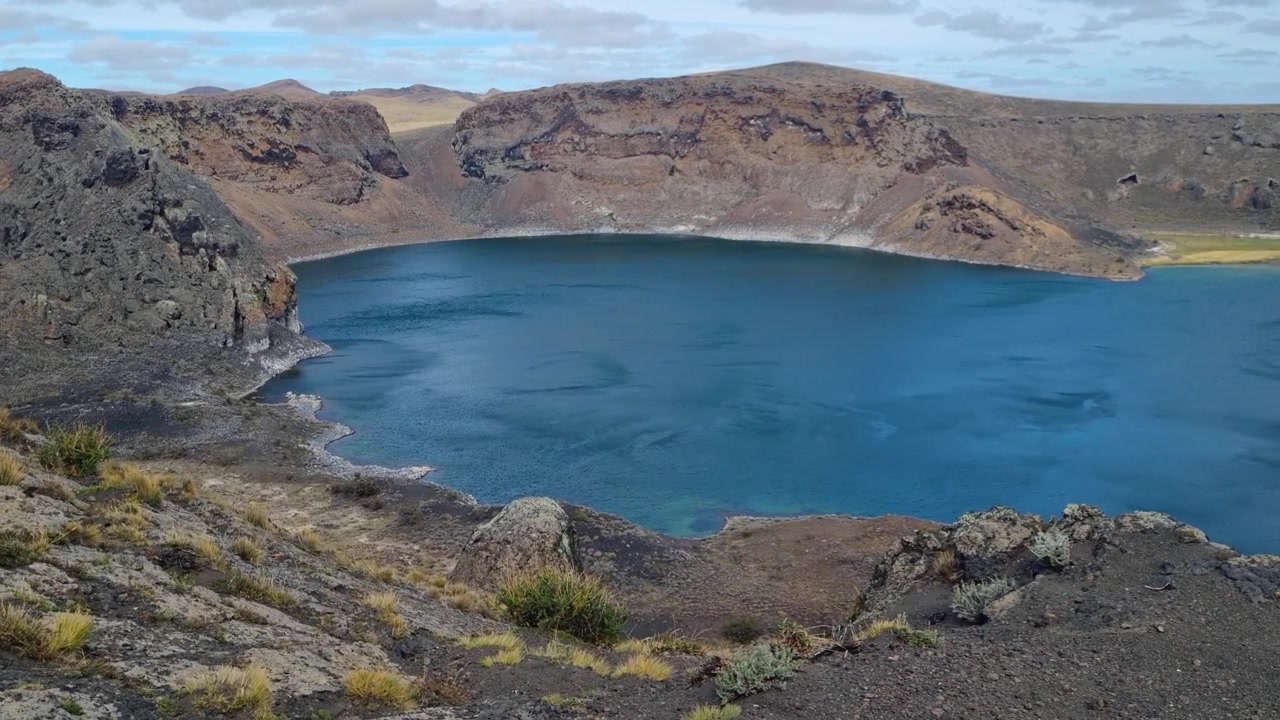 Laguna Azul, um impressionante lago de cratera vulcânica na Patagônia, perto de Río Gallegos, Argentina. Ventos agitam suas águas azuis vívidas em meio a paisagens acidentadas, tornando-o um destino cênico para viagens de carro e turismo.