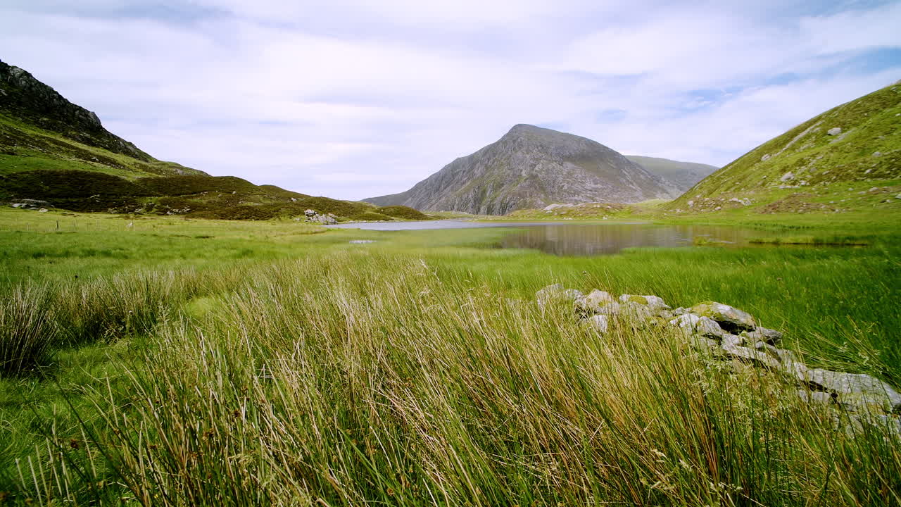 Beautiful green grass meadow and mountain landscape with lake Llyn Idwal and countryside scenery in background, Wales