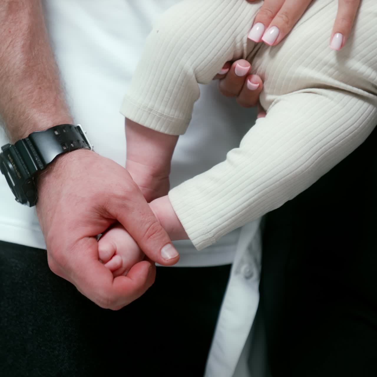 Mother holds her newborn child in hands. Father rubbing sweet little infant feet tenderly. Close up