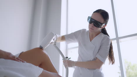 Laser-epilation-and-cosmetology-in-beauty-salon.-Cosmetology-spa-and-hair-removal-concept.-Laser-hair-removal-procedure-of-female-legs.-doctor-in-gloves.