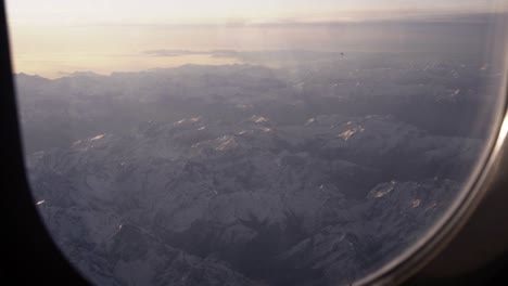 Watching-out-of-a-airplane-window-onto-snowy-mountains-during-sunrise